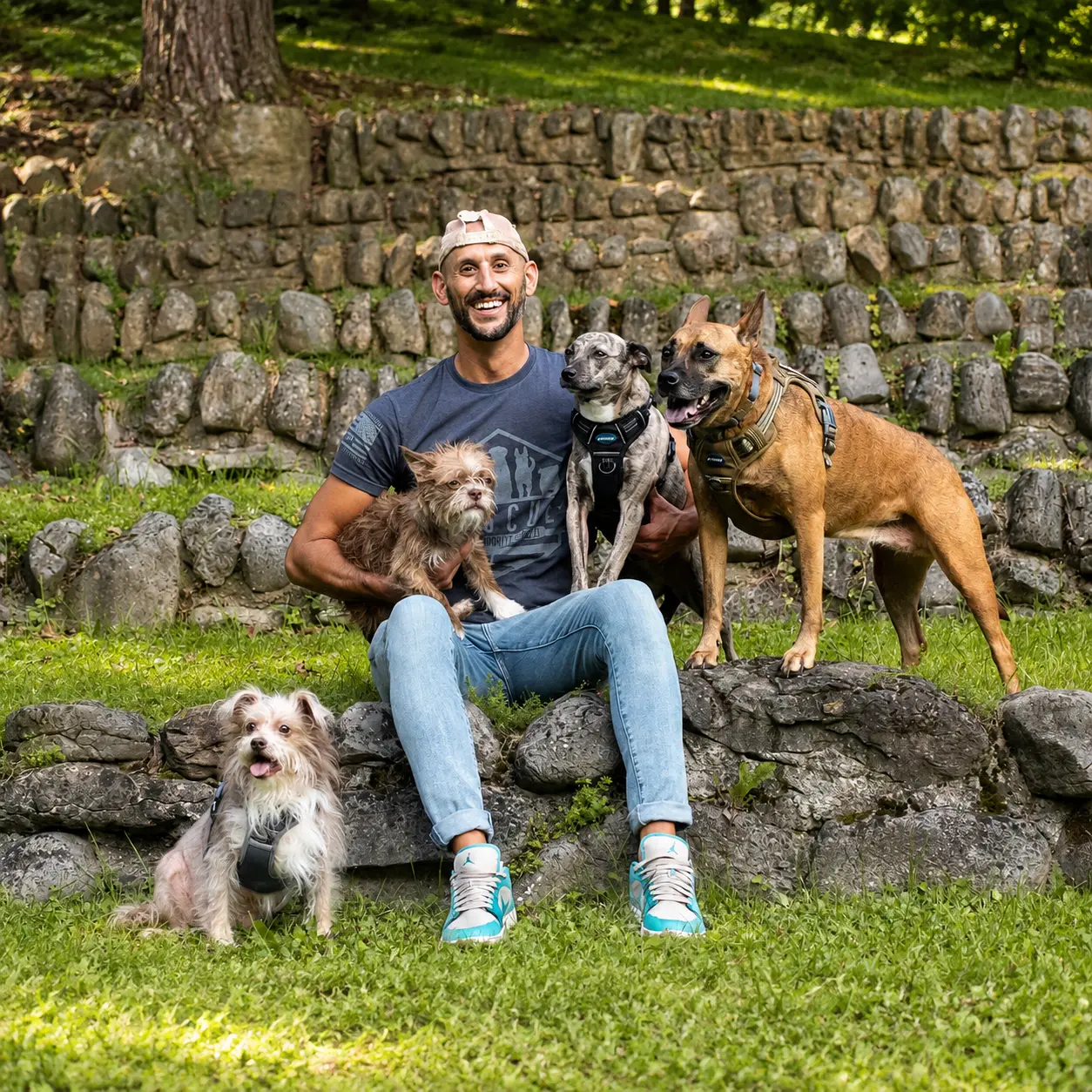 Joseph sitting on a stone wall in the park surrounded by four of his rescue dogs