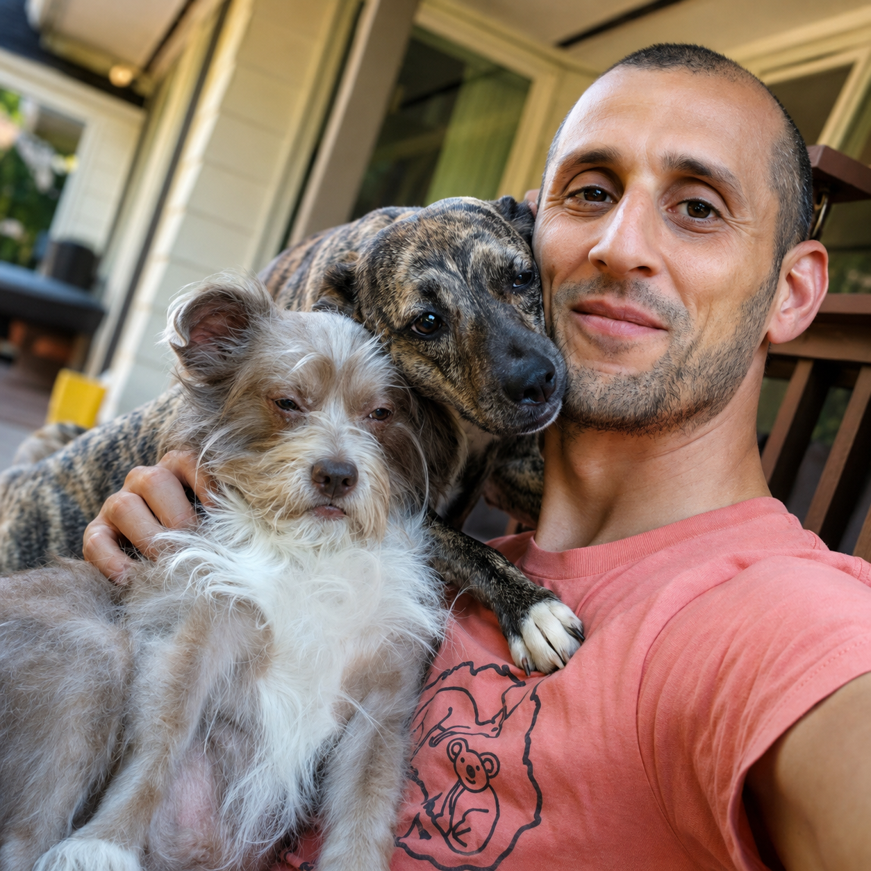 Joseph on the back porch holding his scruffy terrier while his brindle dog leans against his cheek