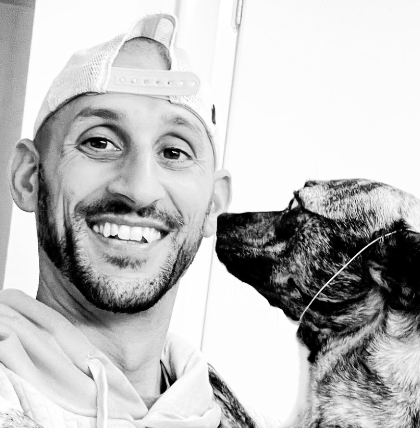Black and white portrait of Joseph smiling beside his shepherd mix