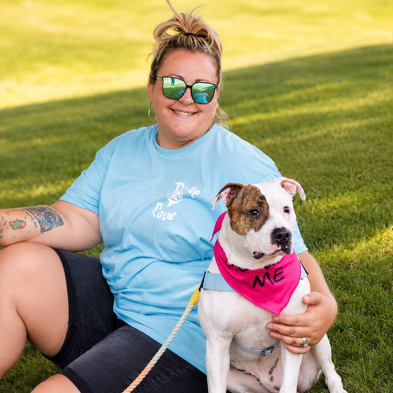 Cristie sitting in the grass with a white and brindle pit bull in a pink adopt me bandana