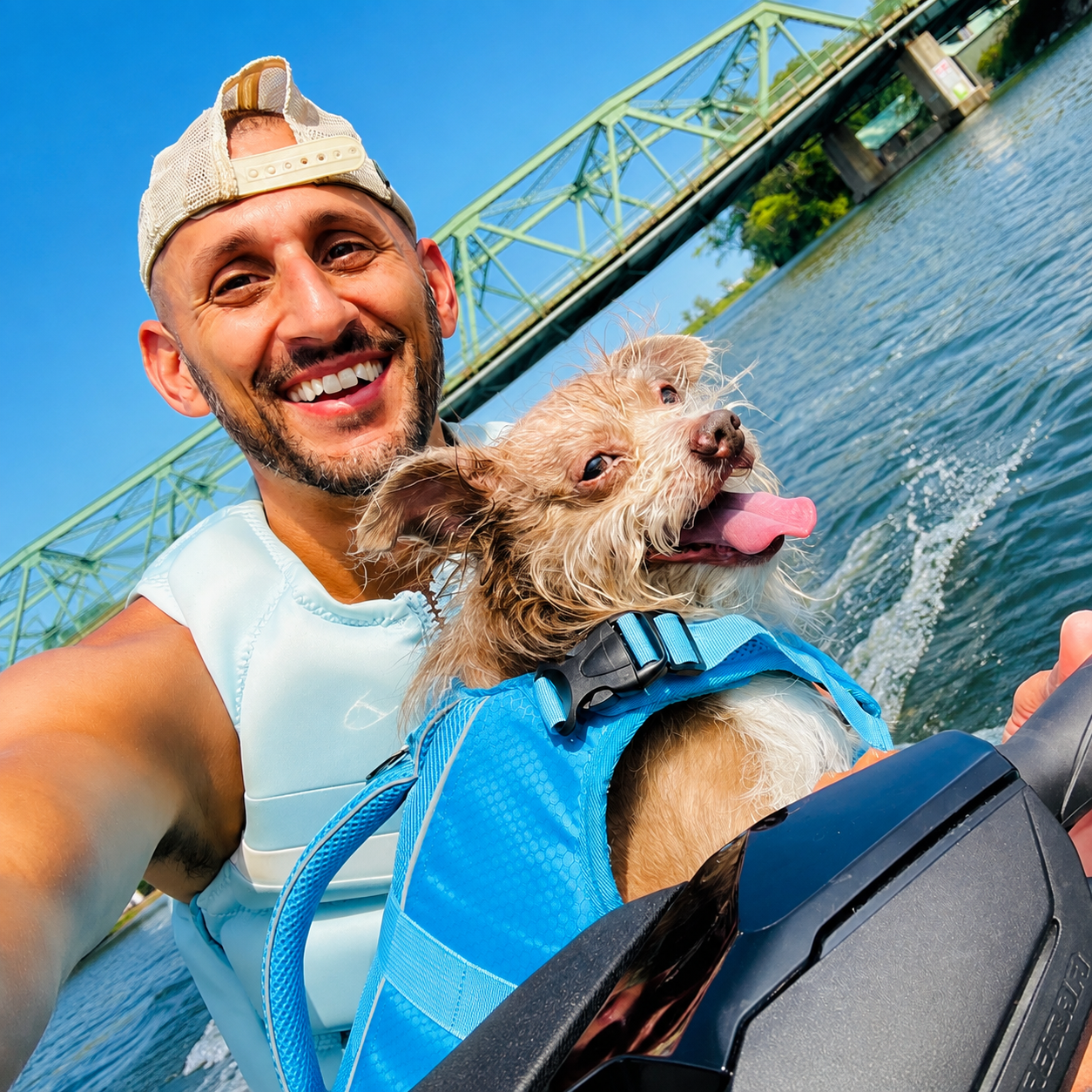 Joseph and his rescue dog in life vests on a jet ski under a green bridge