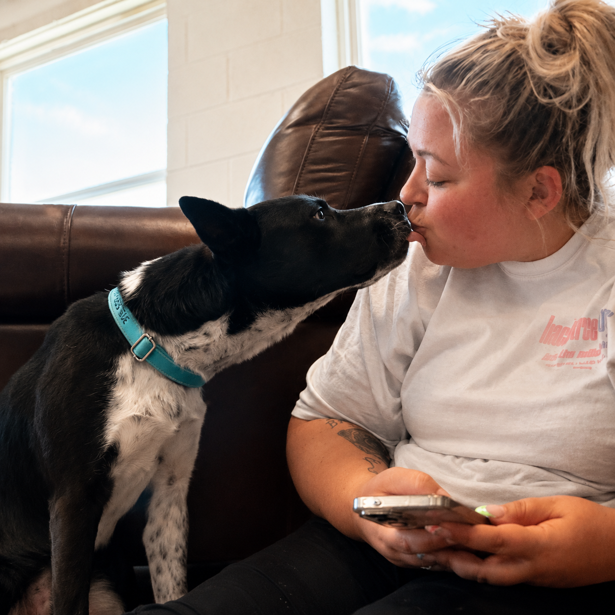 Cristie getting a kiss from a black and white rescue dog on the couch